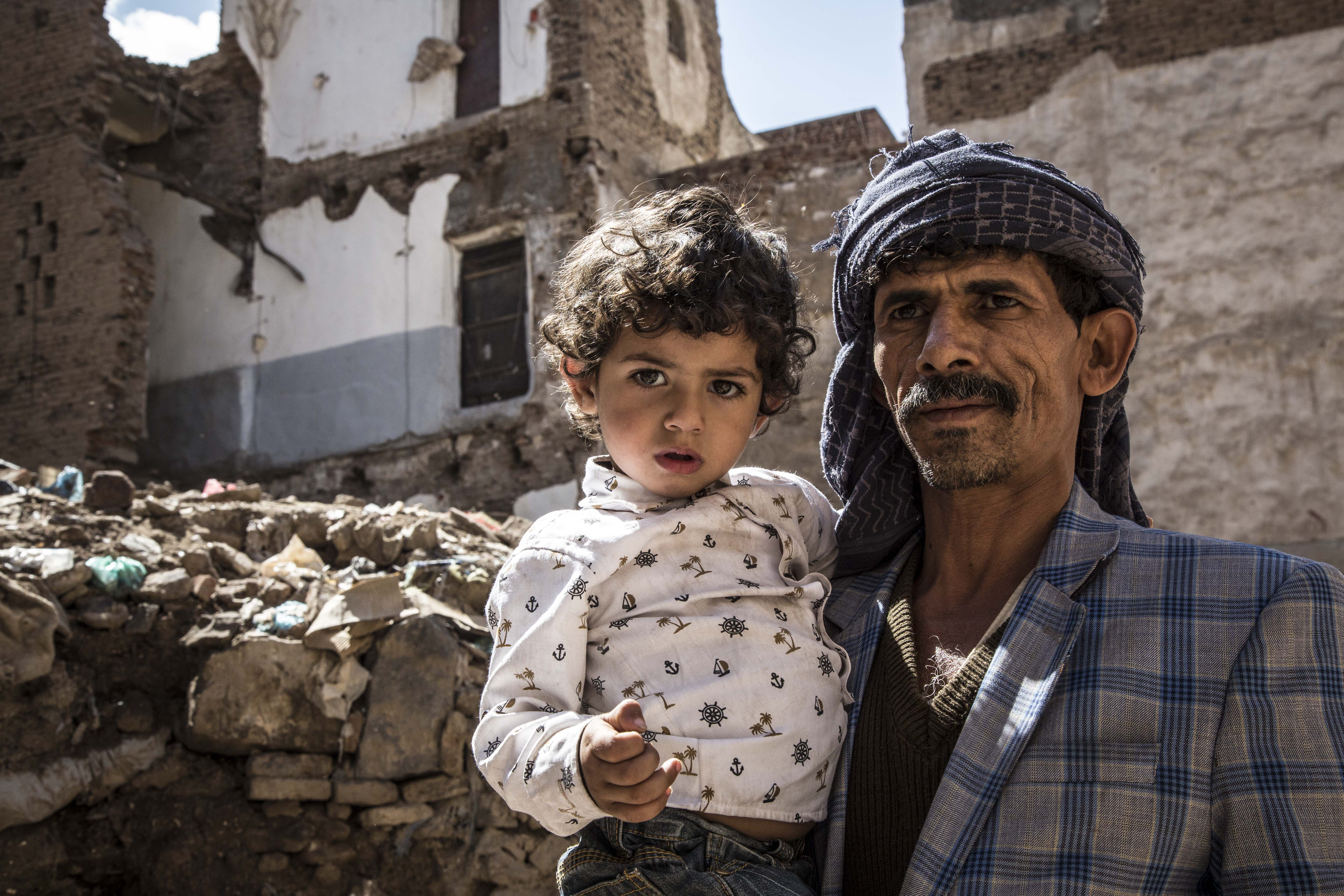 Yemeni father holding his daughter in front of a destroyed building